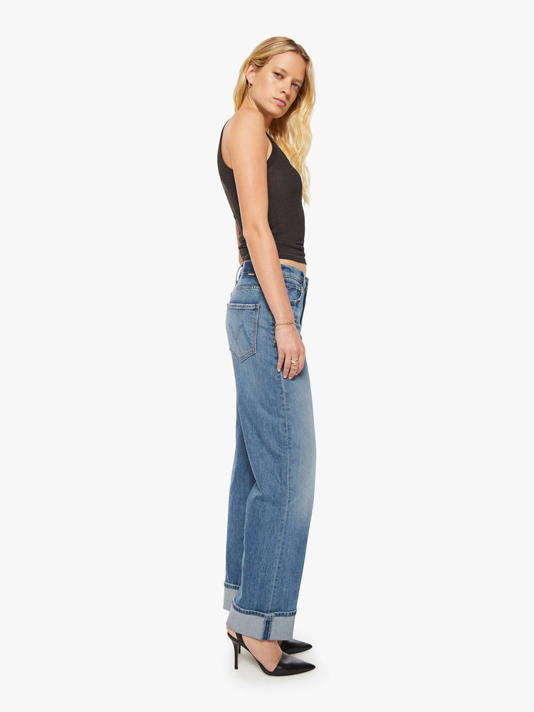 Side view of woman in a mid blue wash jean designed to sit lower on the hips with a loose straight leg and a 31-inch inseam with a clean cuffed hem.