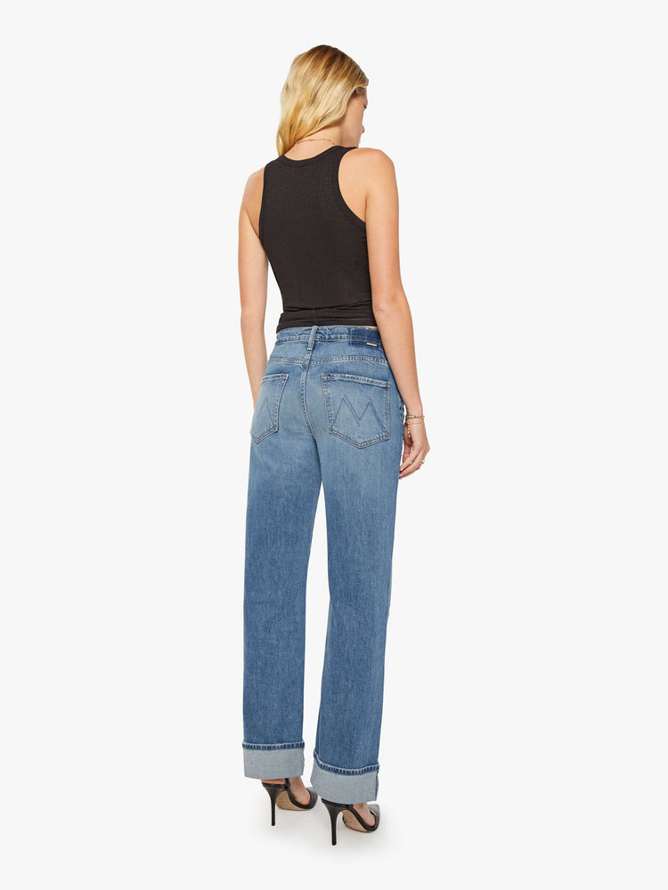 Back view of woman in a mid blue wash jean designed to sit lower on the hips with a loose straight leg and a 31-inch inseam with a clean cuffed hem.