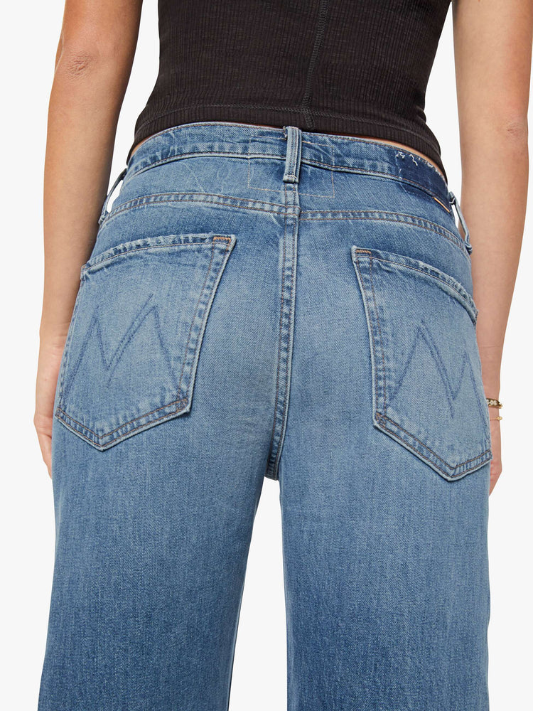 Close up view of woman in a mid blue wash jean designed to sit lower on the hips with a loose straight leg and a 31-inch inseam with a clean cuffed hem.