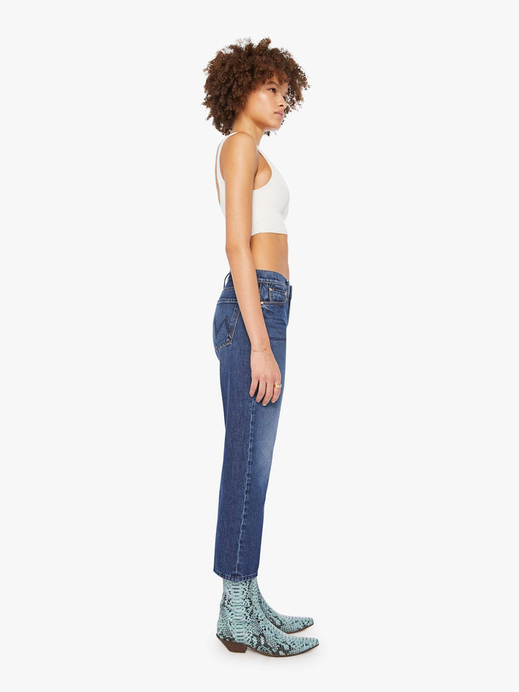 Side view of a woman in a dark blue  high-rise skinny-straight jeans have a zip fly, an ankle-length inseam and a clean hem. 