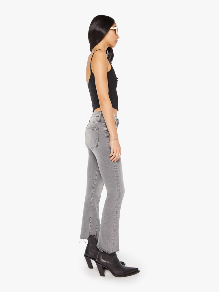 Side view of a woman in a light grey  high-waisted bootcut features seamed details down the front, a zip fly, ankle-length inseam and a frayed triple step-hem. 