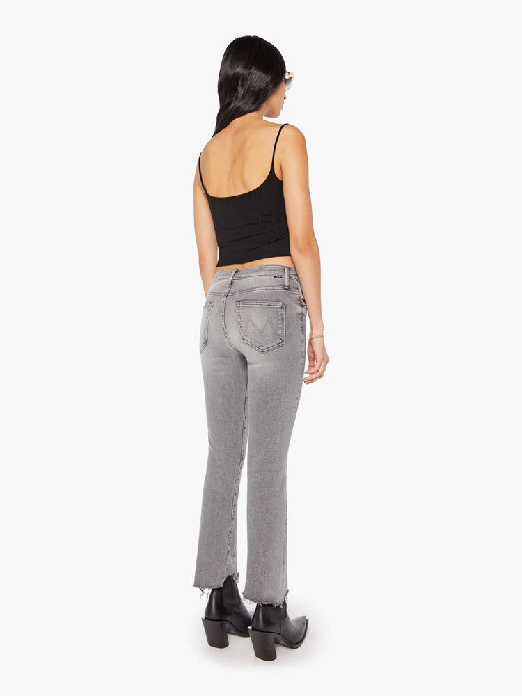 Back view of a woman in a light grey  high-waisted bootcut features seamed details down the front, a zip fly, ankle-length inseam and a frayed triple step-hem. 