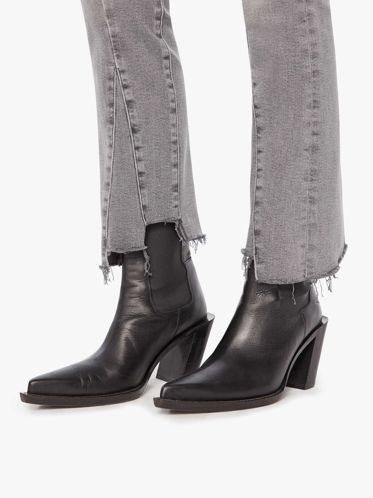 Hem view of a woman in a light grey  high-waisted bootcut features seamed details down the front, a zip fly, ankle-length inseam and a frayed triple step-hem. 