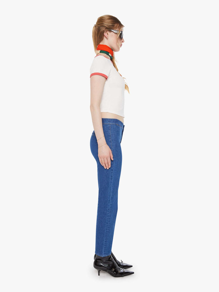 Side  view of a woman in a mid blue straight-leg jeans with a mid rise, zip fly, ankle-length inseam and a clean hem.