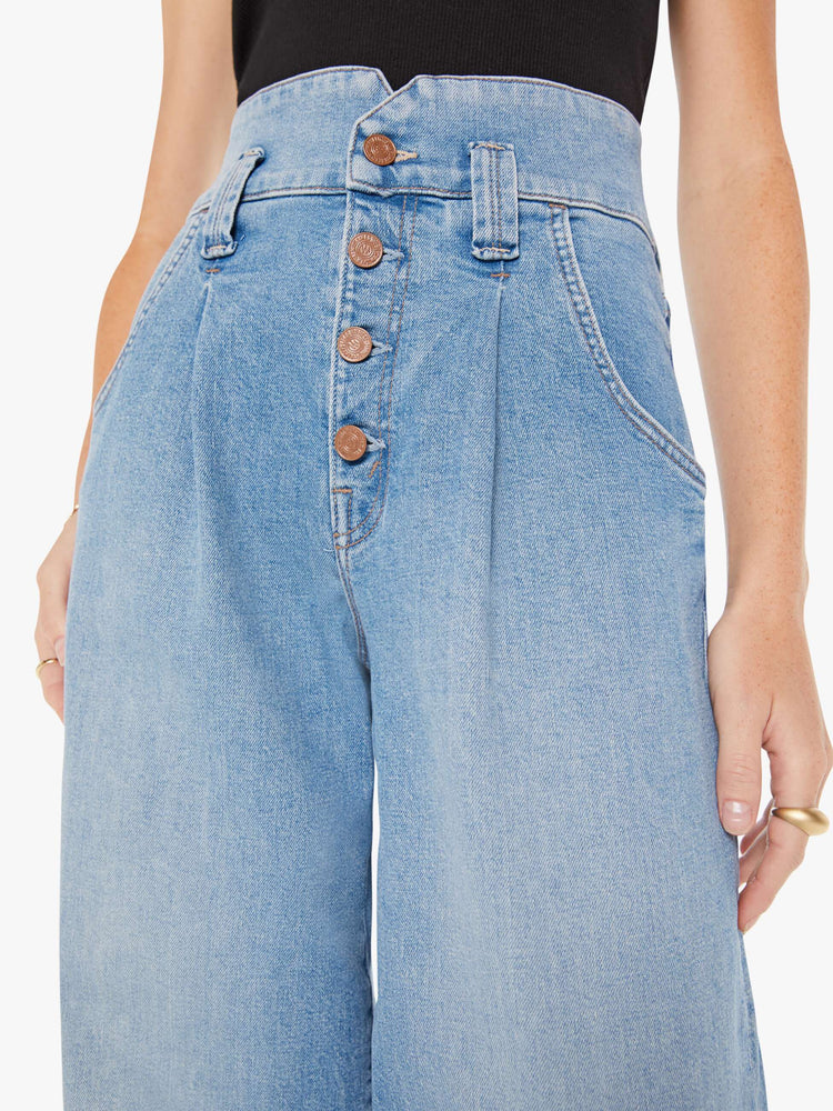 Front close up view of a womens light blue wash jean featuring a super high rise, a wide leg that tapers, and a button fly.