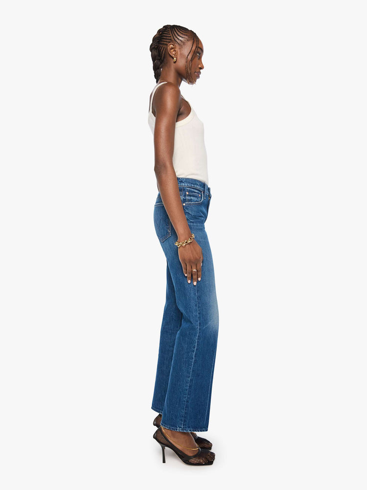 Side view of a woman in mid blue mid-rise jeans with a wide straight leg, zip fly and long 31-inch inseam with a clean hem. 