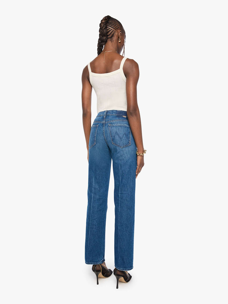 Back view of a woman in mid blue mid-rise jeans with a wide straight leg, zip fly and long 31-inch inseam with a clean hem. 