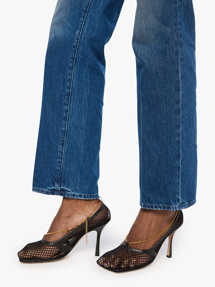 Hem close up view of a woman in mid blue mid-rise jeans with a wide straight leg, zip fly and long 31-inch inseam with a clean hem. 