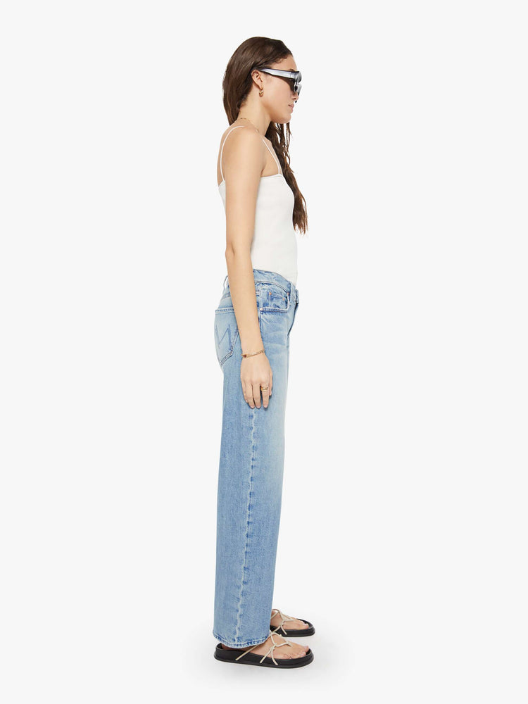 Side view of a woman  in a light blue mid-rise jeans with a wide straight leg, zip fly and long 32-inch inseam with a clean hem.