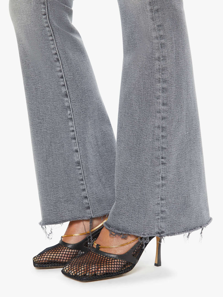 Hem view of a woman in a light grey high-rise flare with a zip fly, 31-inch inseam and a frayed hem.