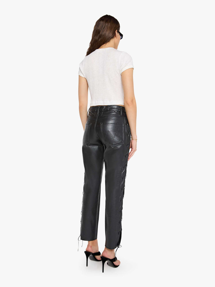 Back view of a woman in black leather high waisted pants with a zip fly, straight leg, 29-inch inseam and a lace-up detail on the outer seams.