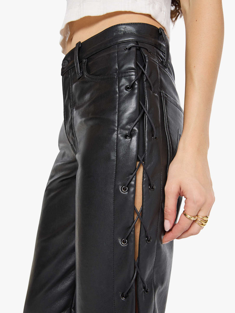 Close up view of a woman in black leather high waisted pants with a zip fly, straight leg, 29-inch inseam and a lace-up detail on the outer seams.