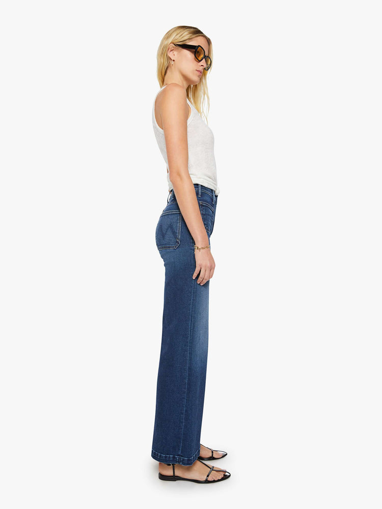 Side view of a woman in a dark blue wide leg jeans with a high rise, zip fly, patch pockets, 32-inch inseam and clean hem.