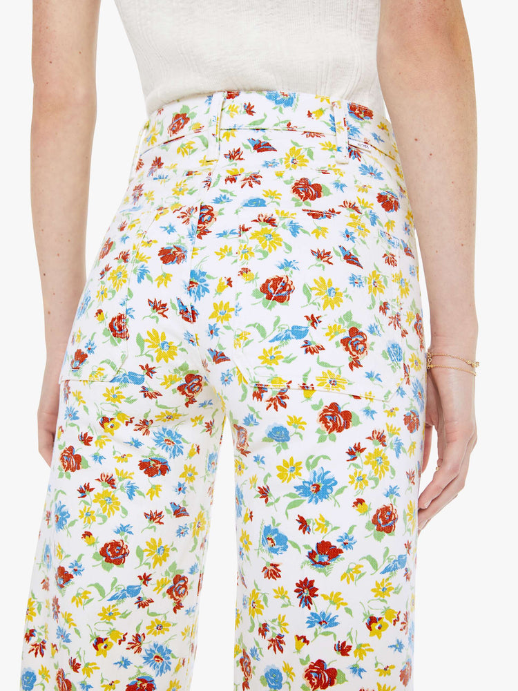 Close up view of a woman in a bright white with colorful flowers wide leg jeans with a high rise, zip fly, patch pockets, 32-inch inseam and clean hem. 