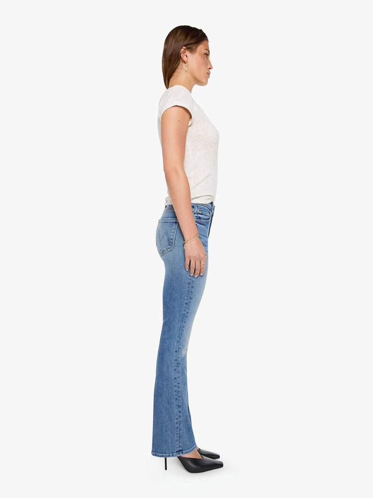 Side view of a woman in mid blue bootcut jeans with a mid rise, zip fly and a long 31-inch inseam with a clean hem.