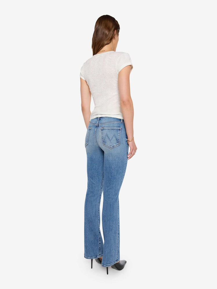 Back view of a woman in mid blue bootcut jeans with a mid rise, zip fly and a long 31-inch inseam with a clean hem.