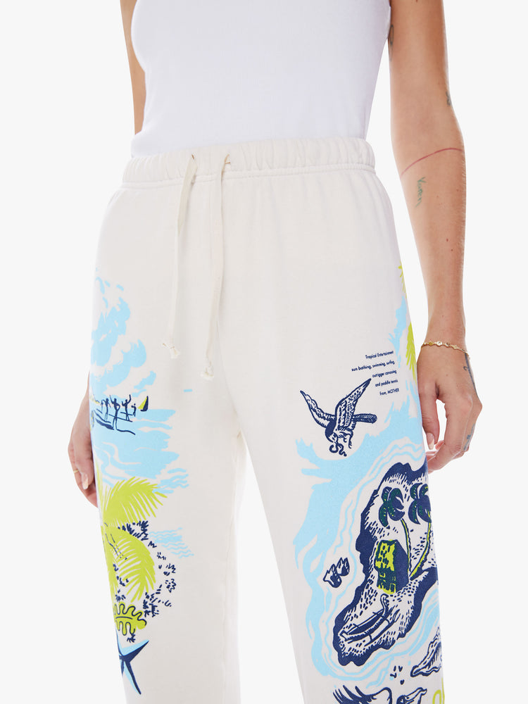 Close up waist view of a woman high-rise drawstring waist and an ankle-length inseam with elastic hems sweatpants in off-white hue with a blue and green graphic.