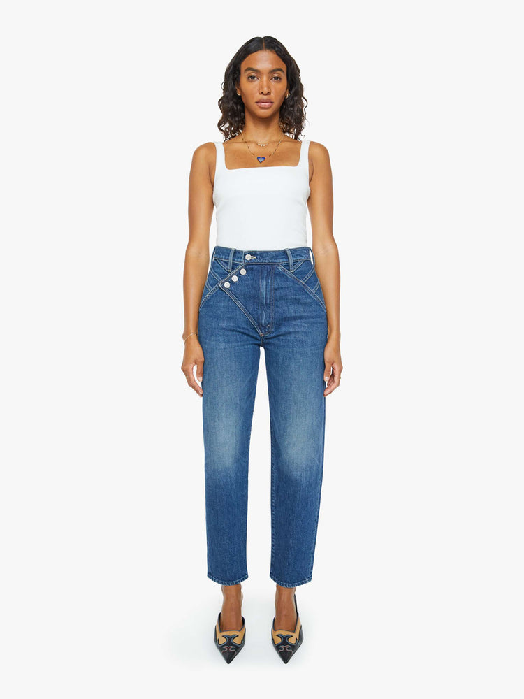 Front view of a woman in a mid blue super high-rise straight-leg jeans with a buttoned flap at the waistband, angled seamed details and a 29-inch inseam with a clean hem.