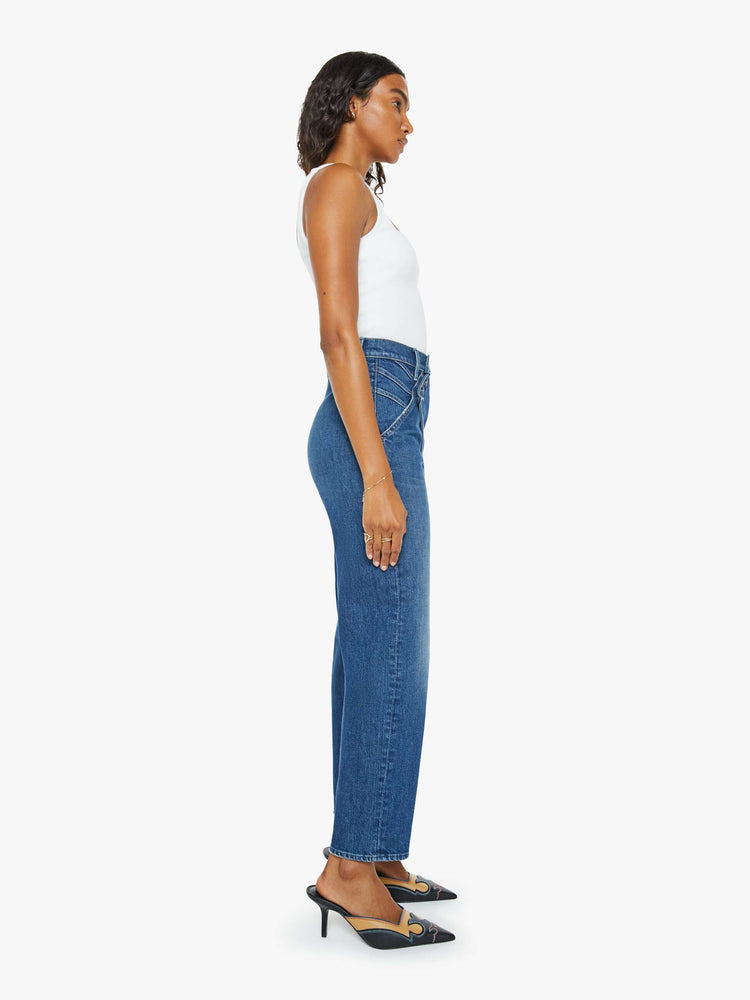 Side view of a woman in a mid blue super high-rise straight-leg jeans with a buttoned flap at the waistband, angled seamed details and a 29-inch inseam with a clean hem.