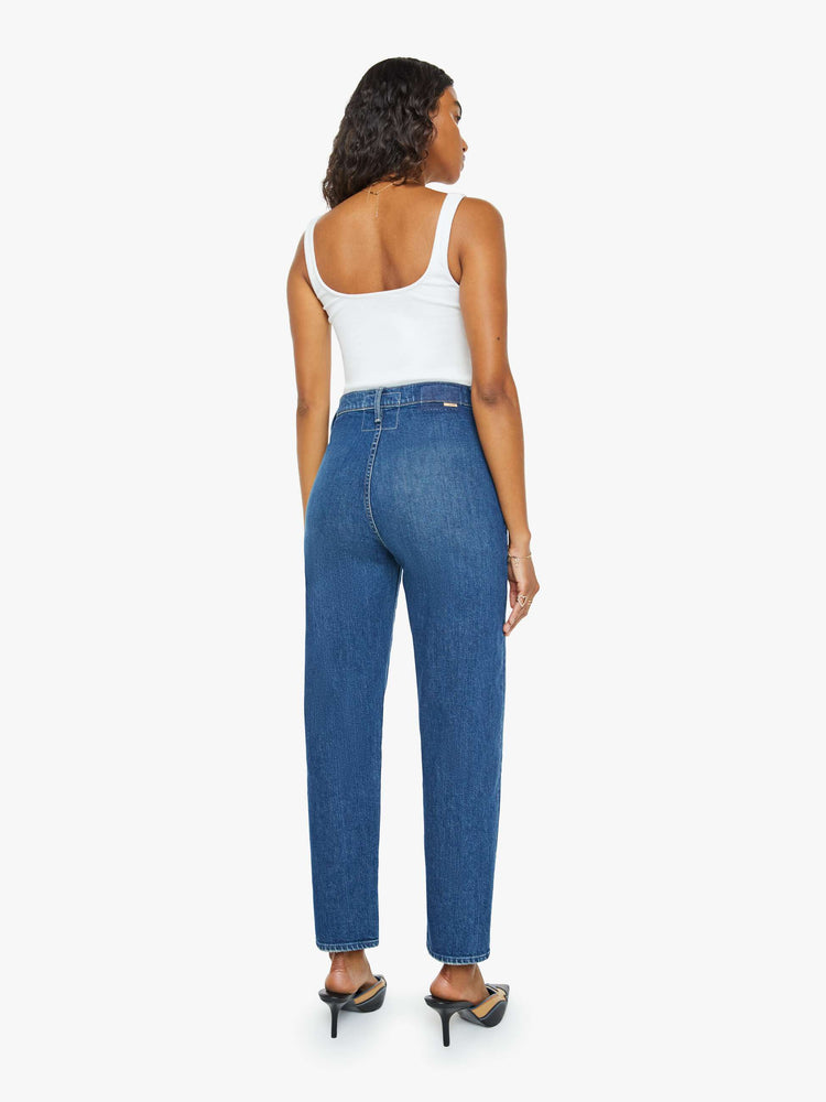 Back view of a woman in a mid blue super high-rise straight-leg jeans with a buttoned flap at the waistband, angled seamed details and a 29-inch inseam with a clean hem.