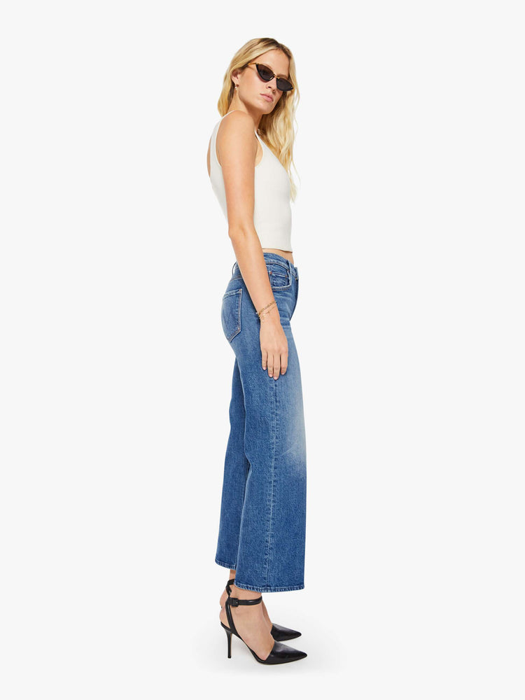 Side view of a woman in a med blue mid-rise jeans with a loose fit, wide leg, zip fly and a 28.25-inch inseam with a clean hem.