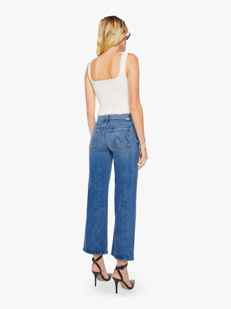 Back view of a woman in a med blue mid-rise jeans with a loose fit, wide leg, zip fly and a 28.25-inch inseam with a clean hem.