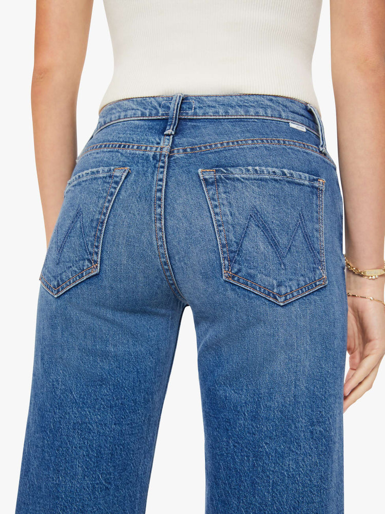 Close up view of a woman in a med blue mid-rise jeans with a loose fit, wide leg, zip fly and a 28.25-inch inseam with a clean hem.