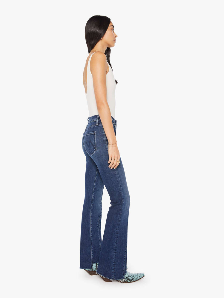 Side view of a woman in a dark blue high-waisted bootcut features a zip fly, seamed details down the front, a 31-inch inseam and a frayed triple step-hem.