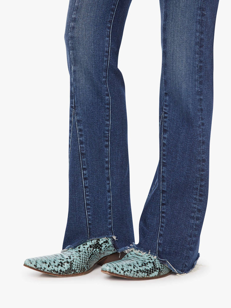 Hem view of a woman in a dark blue high-waisted bootcut features a zip fly, seamed details down the front, a 31-inch inseam and a frayed triple step-hem.