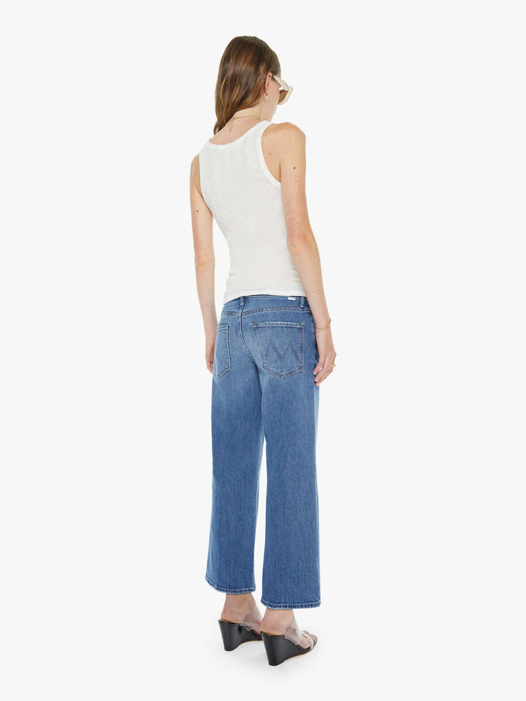 Back view of a woman in a mid blue mid-rise jeans with a loose fit, wide leg, zip fly and ankle-length inseam with a clean hem.