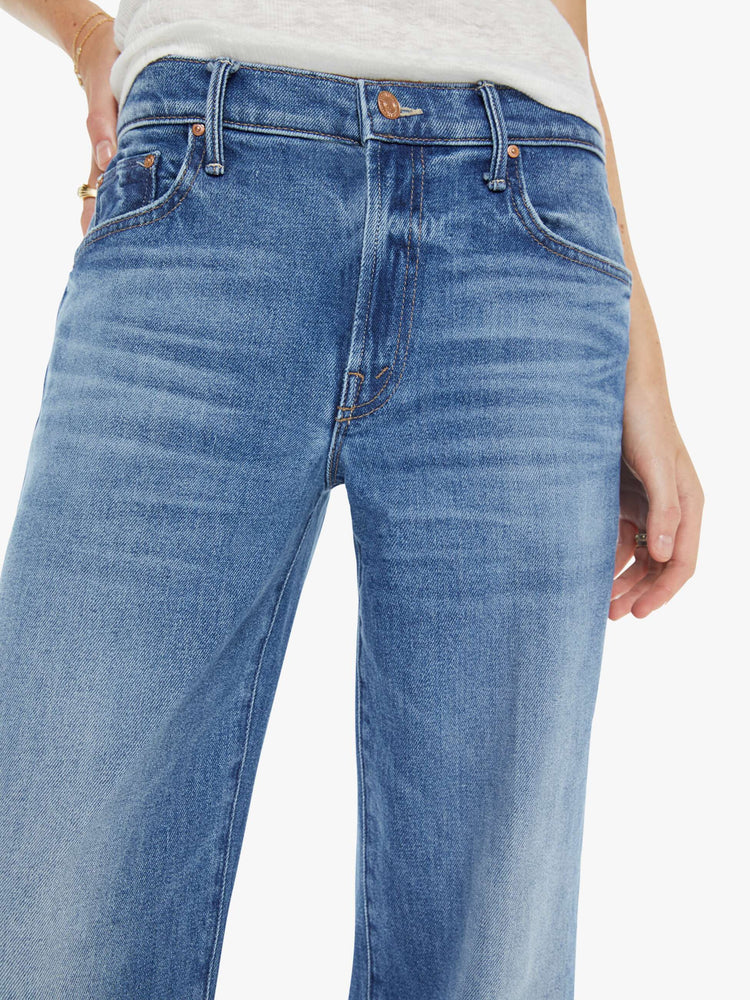 Close up view of a woman in a mid blue mid-rise jeans with a loose fit, wide leg, zip fly and ankle-length inseam with a clean hem.