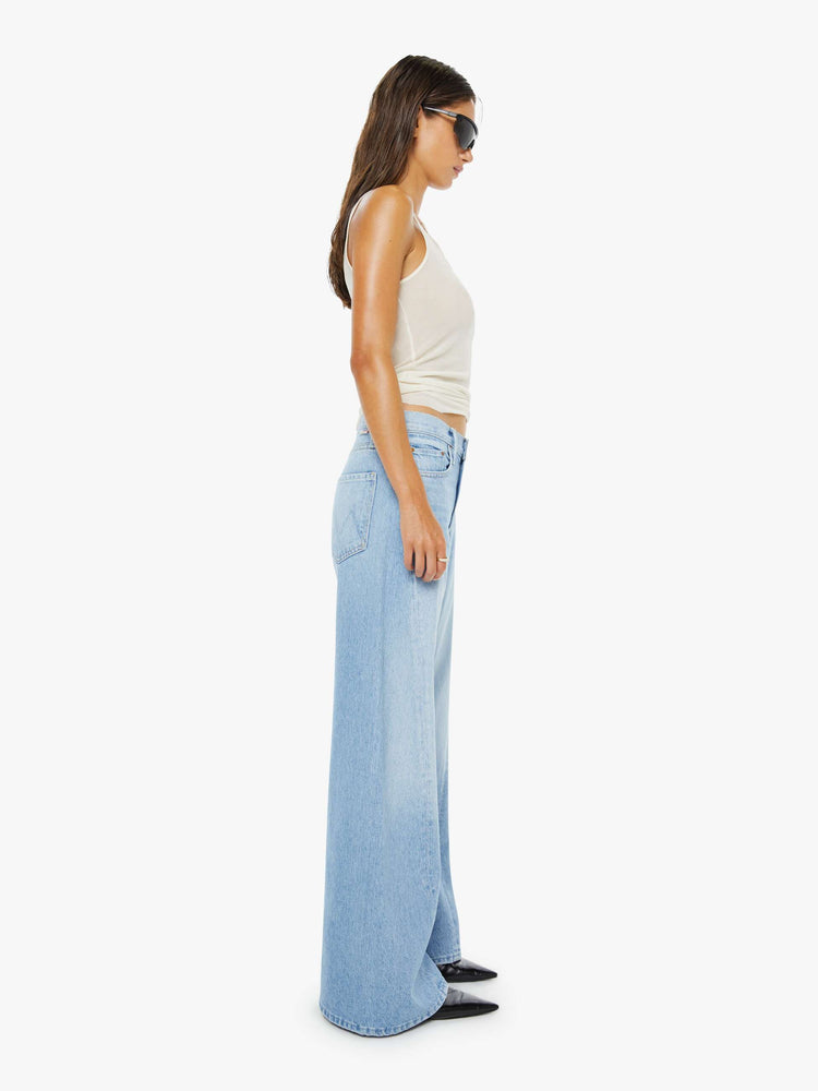 Side view of a woman in a light blue  jean designed to sit on the hips with a slouchy fit, high rise,  a zip fly, loose wide leg with a curved outer seam and a 31-inch inseam with a clean hem. 