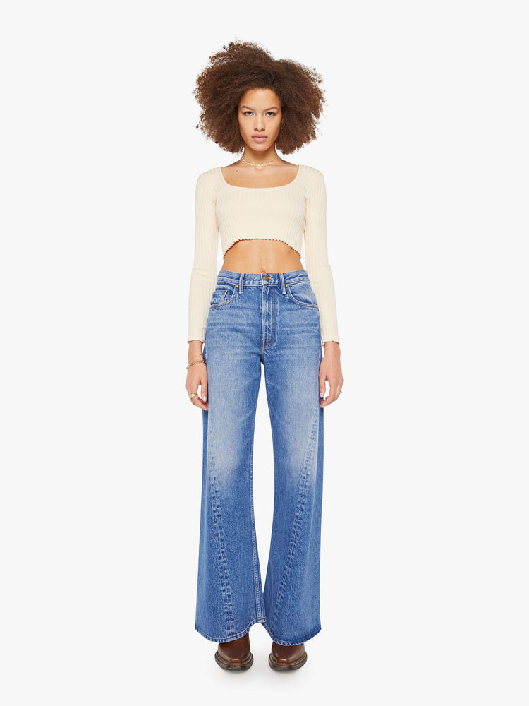 Front view of  woman in a mid blue high waisted jean with a wide leg  with a curved outer seam and a long 33.5-inch inseam with a clean hem. 