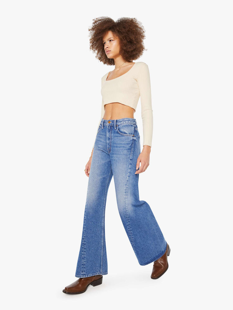 Walking view of  woman in a mid blue high waisted jean with a wide leg  with a curved outer seam and a long 33.5-inch inseam with a clean hem. 