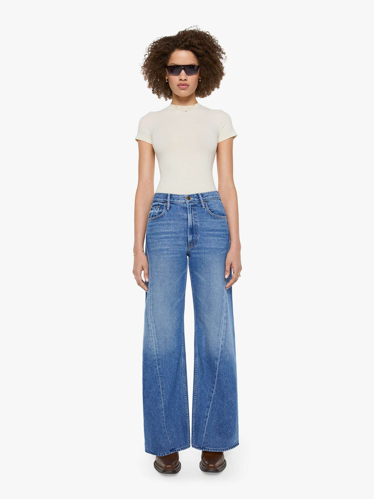 Front view of  woman in a mid blue high waisted jean with a wide leg  with a curved outer seam and a long 33.5-inch inseam with a clean hem.