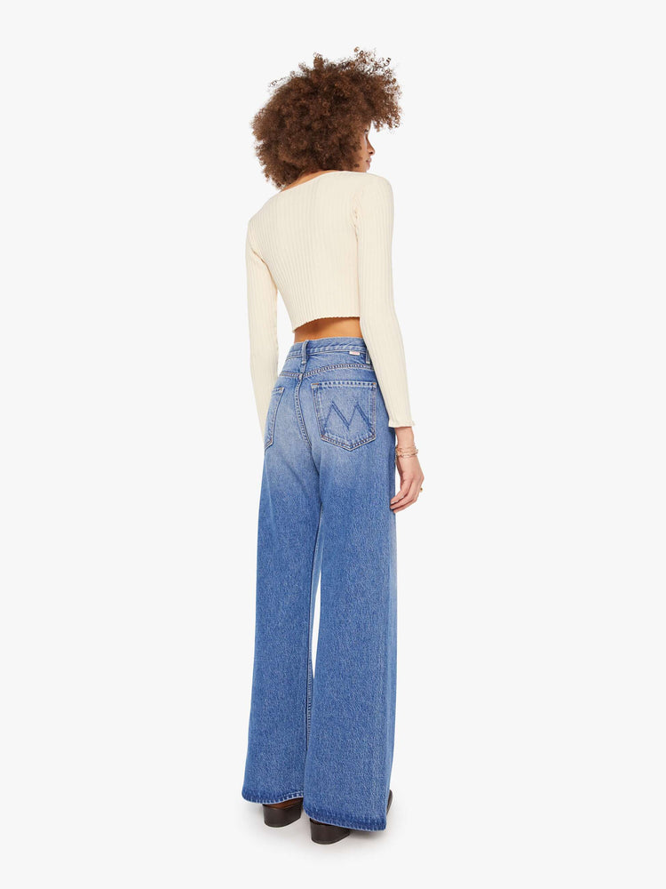 Back view of  woman in a mid blue high waisted jean with a wide leg  with a curved outer seam and a long 33.5-inch inseam with a clean hem. 