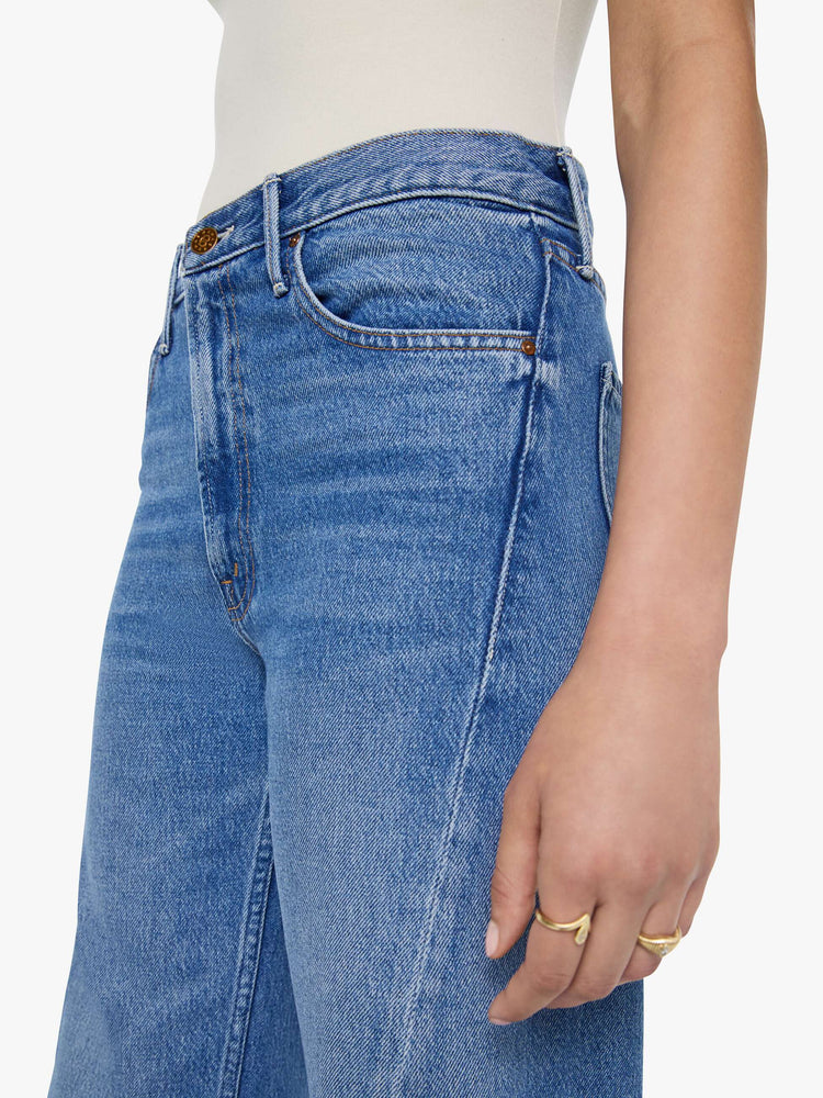 Close up view of  woman in a mid blue high waisted jean with a wide leg  with a curved outer seam and a long 33.5-inch inseam with a clean hem. 