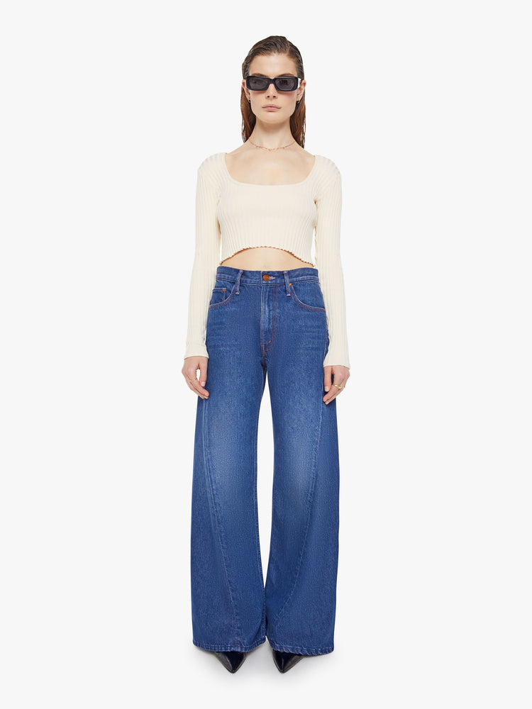 Front view of woman in a mid blue super high rise jeans have a zip fly, loose wide leg with a curved outer seam and a long inseam with a clean hem.