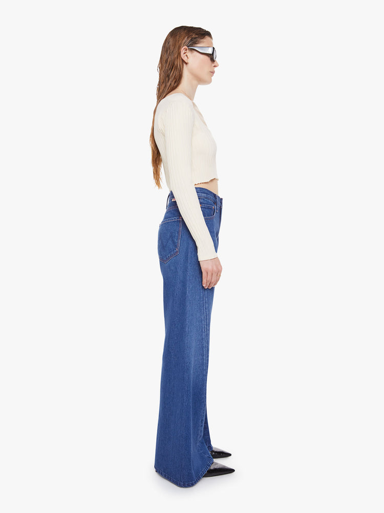 Side view of woman in a mid blue super high rise jeans have a zip fly, loose wide leg with a curved outer seam and a long inseam with a clean hem.