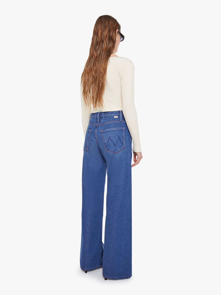 Back view of woman in a mid blue super high rise jeans have a zip fly, loose wide leg with a curved outer seam and a long inseam with a clean hem.