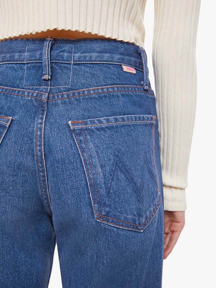 Back view of woman in a mid blue super high rise jeans have a zip fly, loose wide leg with a curved outer seam and a long inseam with a clean hem.