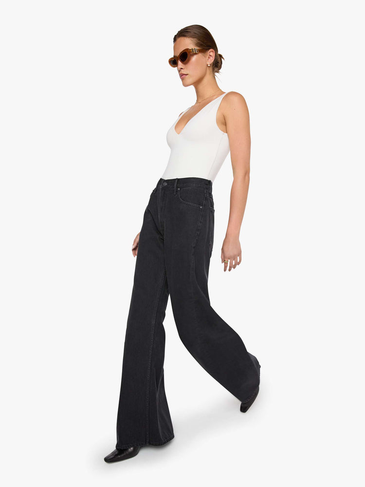 Walking view of  woman in a black high waisted jean with a wide leg  with a curved outer seam and a long 32 inch inseam with a clean hem.