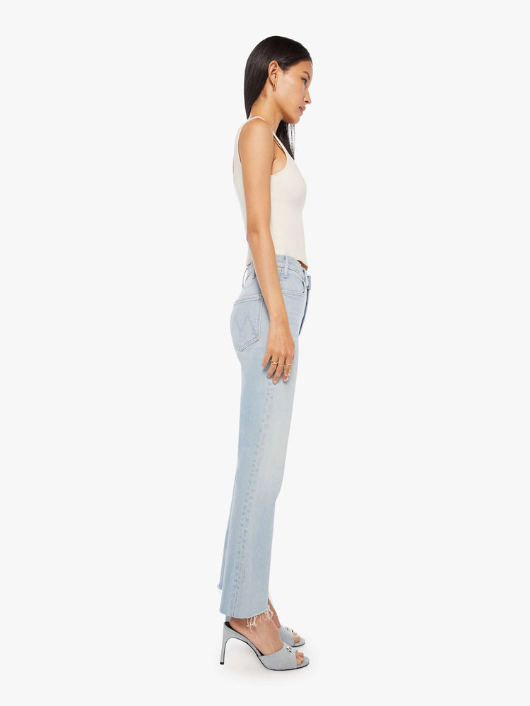 Side view of a woman in a light blue high-rise flare has an ankle-length inseam and a raw hem.
