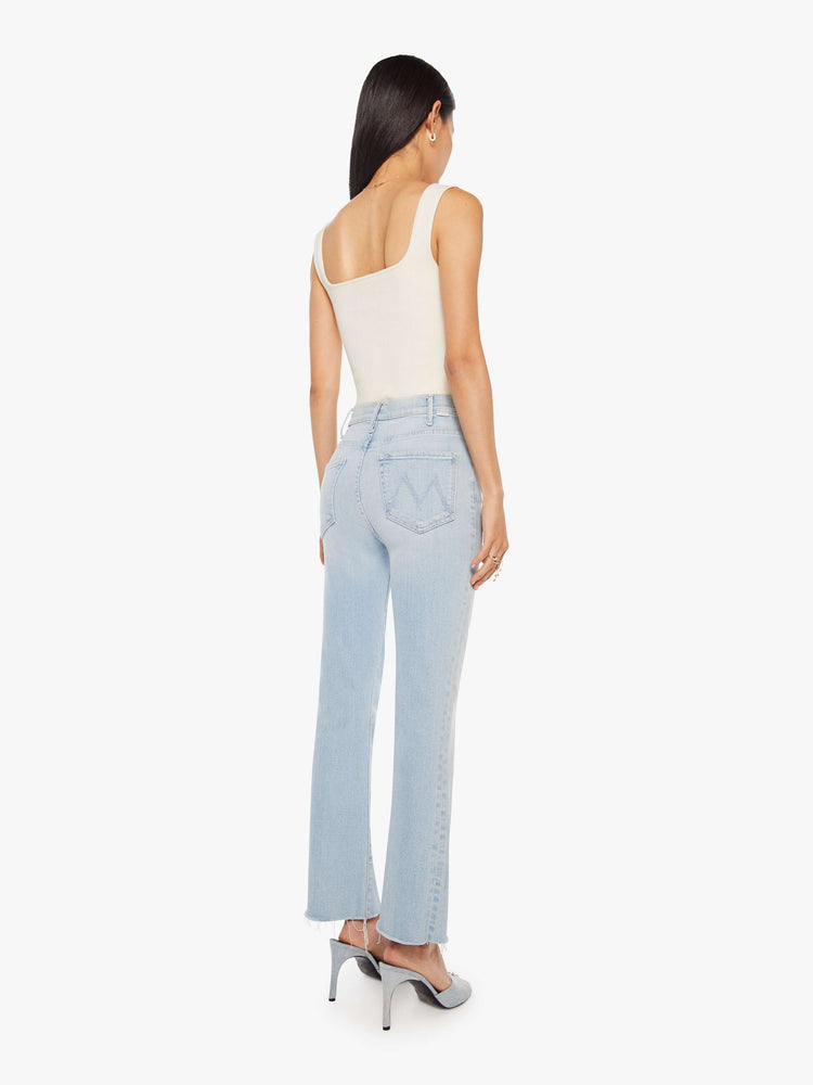 Back view of a woman in a light blue high-rise flare has an ankle-length inseam and a raw hem.