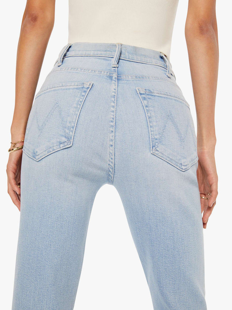 Back view of a woman in a light blue high-rise flare has an ankle-length inseam and a raw hem.