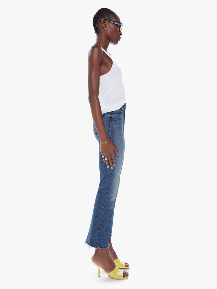 Side view of a womens medium blue wash jean featuring a high rise, flare leg, and a raw ankle length hem.