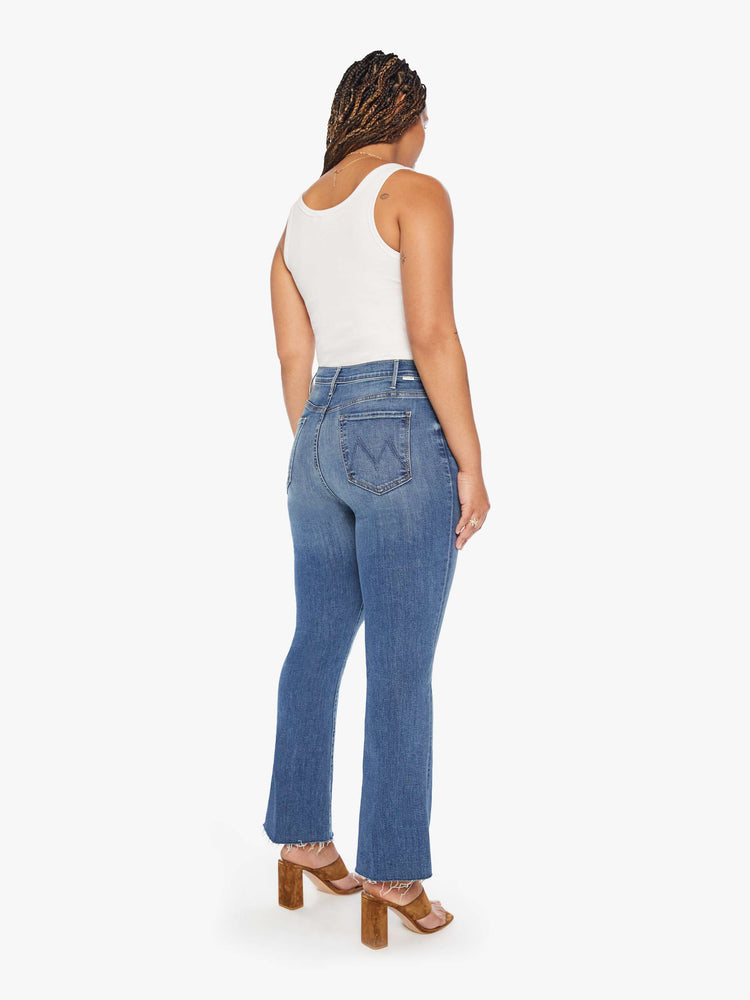 Back view of a womens medium blue wash jean featuring a high rise, flare leg, and a raw ankle length hem.