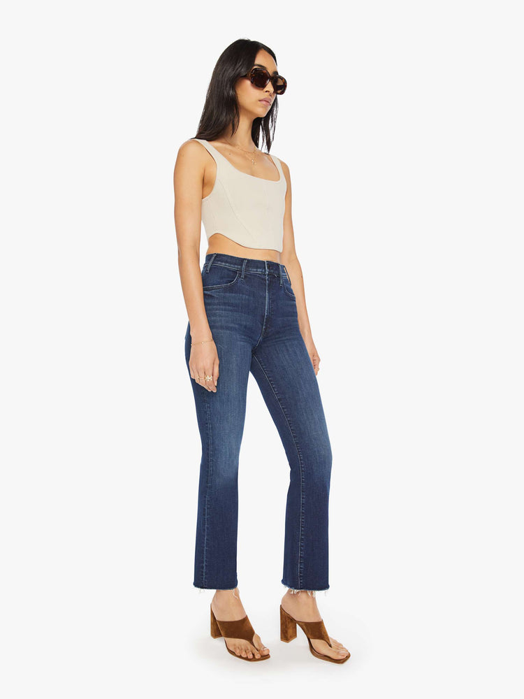 Side angle view of a woman dark blue high-rise flare has an ankle-length inseam and a raw hem.