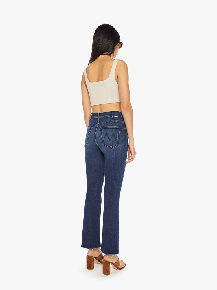 Back view of a woman dark blue high-rise flare has an ankle-length inseam and a raw hem.