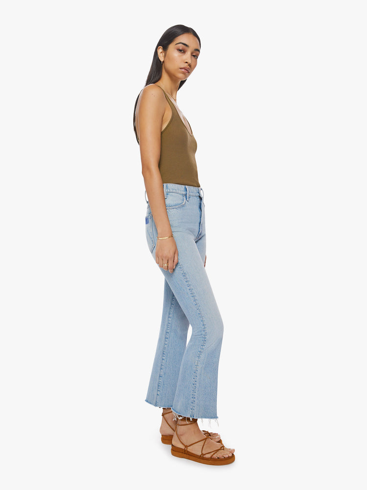 Side angle view of a woman light blue high-rise flare has an ankle-length inseam and a raw hem.